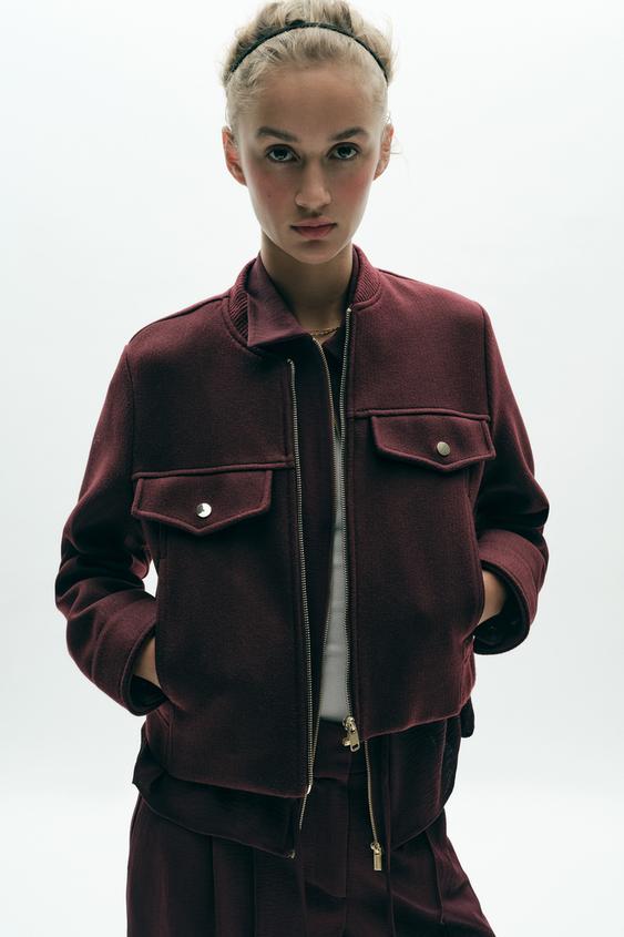 Komplet krátké vínové bundy s kulatým výstřihem, dlouhými rukávy, předními kapsami s klopou a zapínáním na zip.