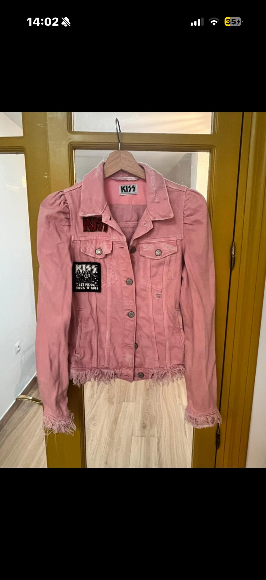 Pink jacket with band patches hanging on a wooden hanger in front of a yellow door. Visible text: "KISS".