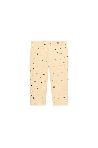 Front view of peach capri pants with studs, mid-rise, front zipper closure, inner button, and metal hooks.