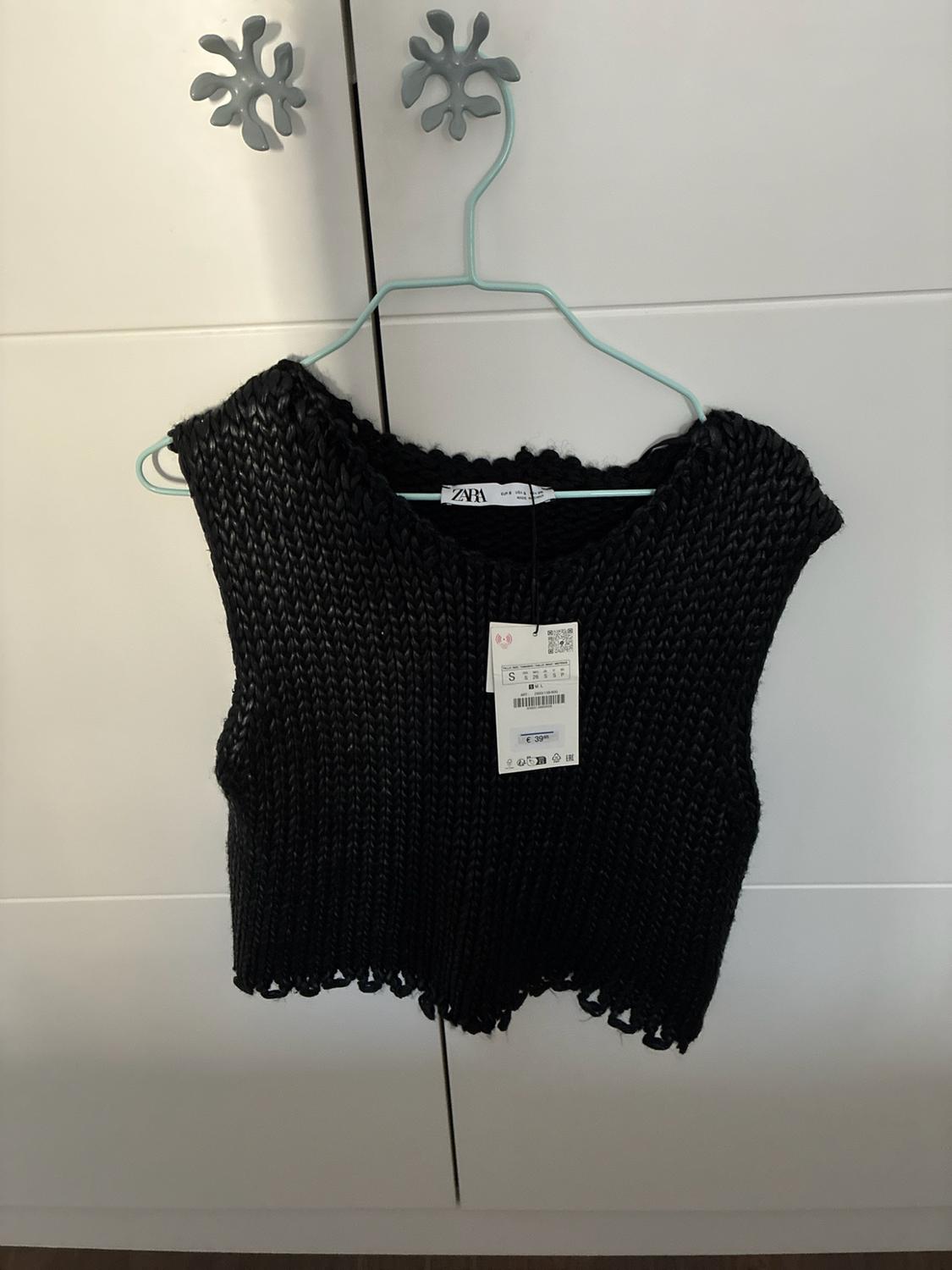 Black chunky knit sleeveless top with an uneven hem hanging in a white wardrobe. Visible text: ZARA, S, €39.95.