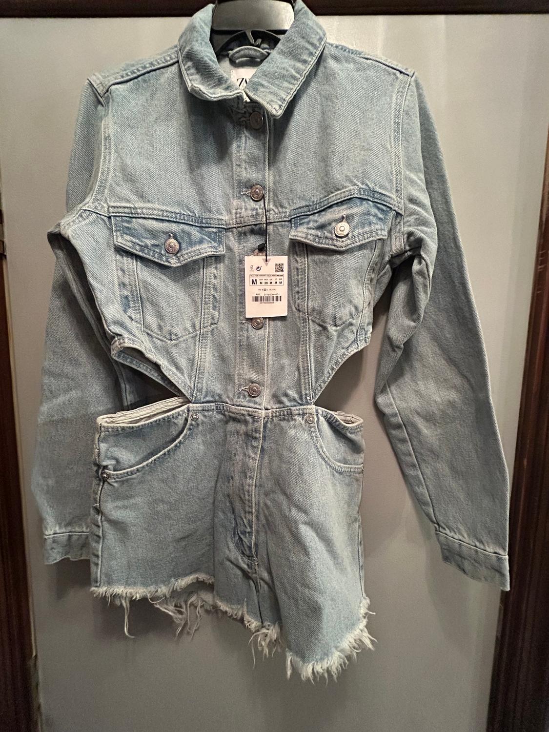 Light blue denim jacket with a cropped design and frayed edges, hanging on a hanger with a visible tag.