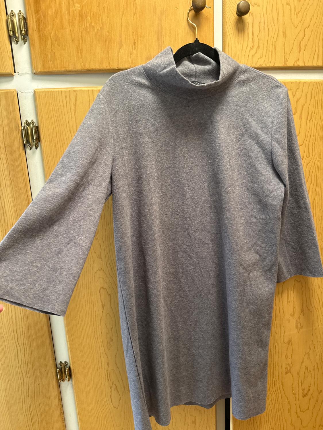 Long-sleeve dress or T-shirt in heather gray with a high neck, hanging from a hanger in front of a wooden wardrobe.