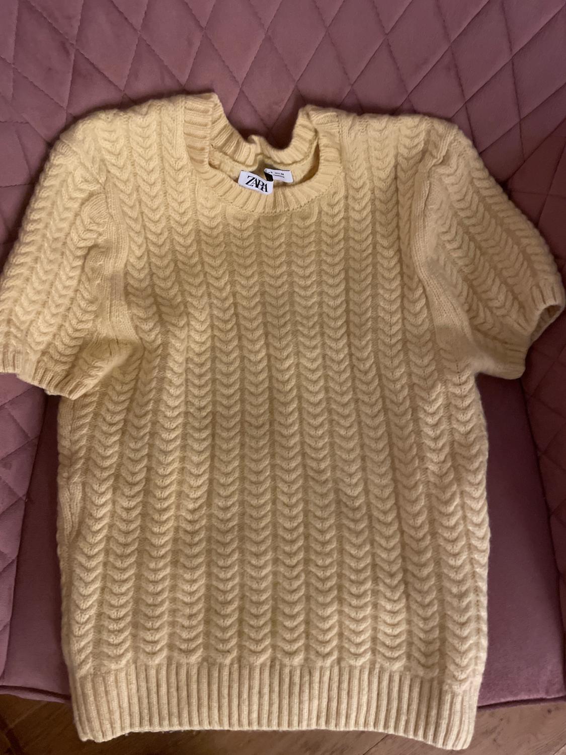Cream cable knit short-sleeved jumper, on a pink upholstered armchair. Visible label: ZARA.