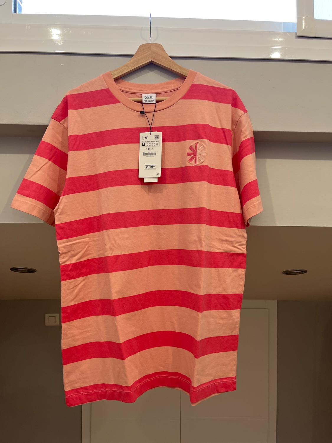 Red and pink horizontal striped T-shirt hanging on a wooden hanger, with price tag visible.