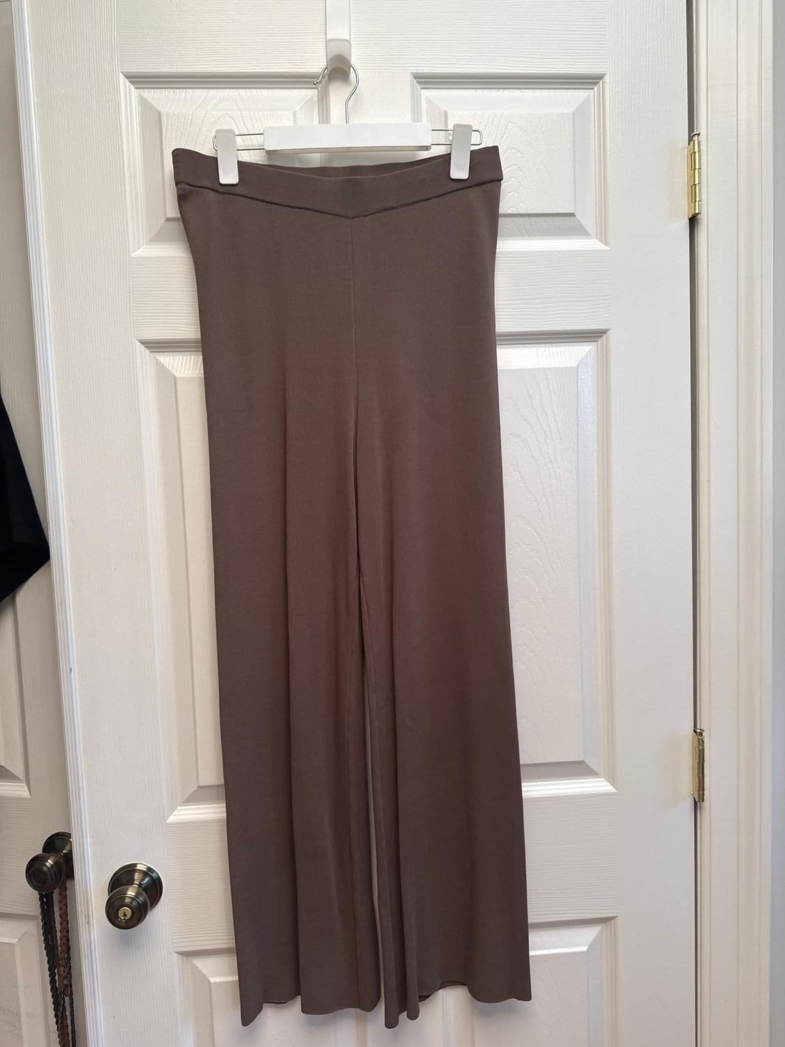 Brown wide-leg trousers hanging on a white hanger over a white door with a metal knob.