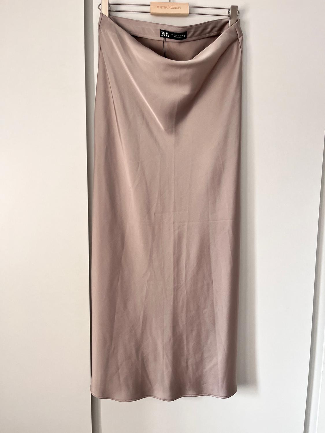 Long beige skirt hanging on a wooden hanger with the visible ZARA brand label. White background.