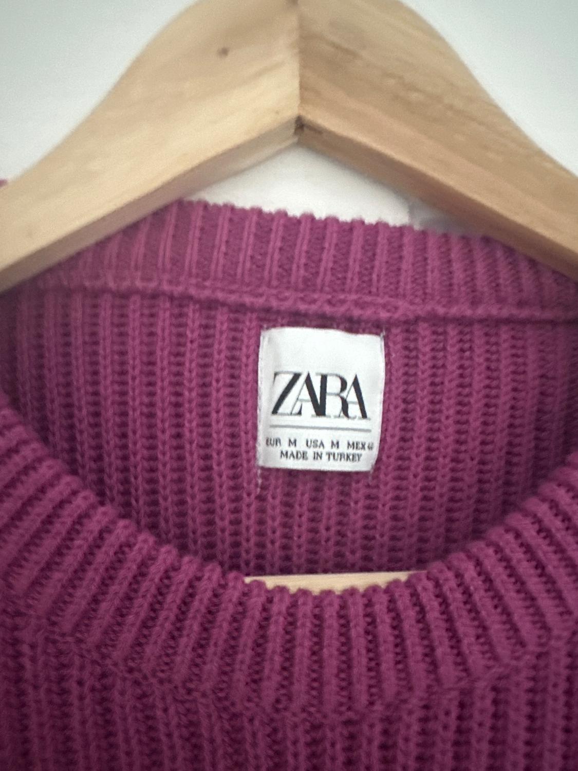 Label of a pink knitted jumper on a wooden hanger. Visible text: "ZARA, EUR M USA M MEX 6, MADE IN TURKEY".