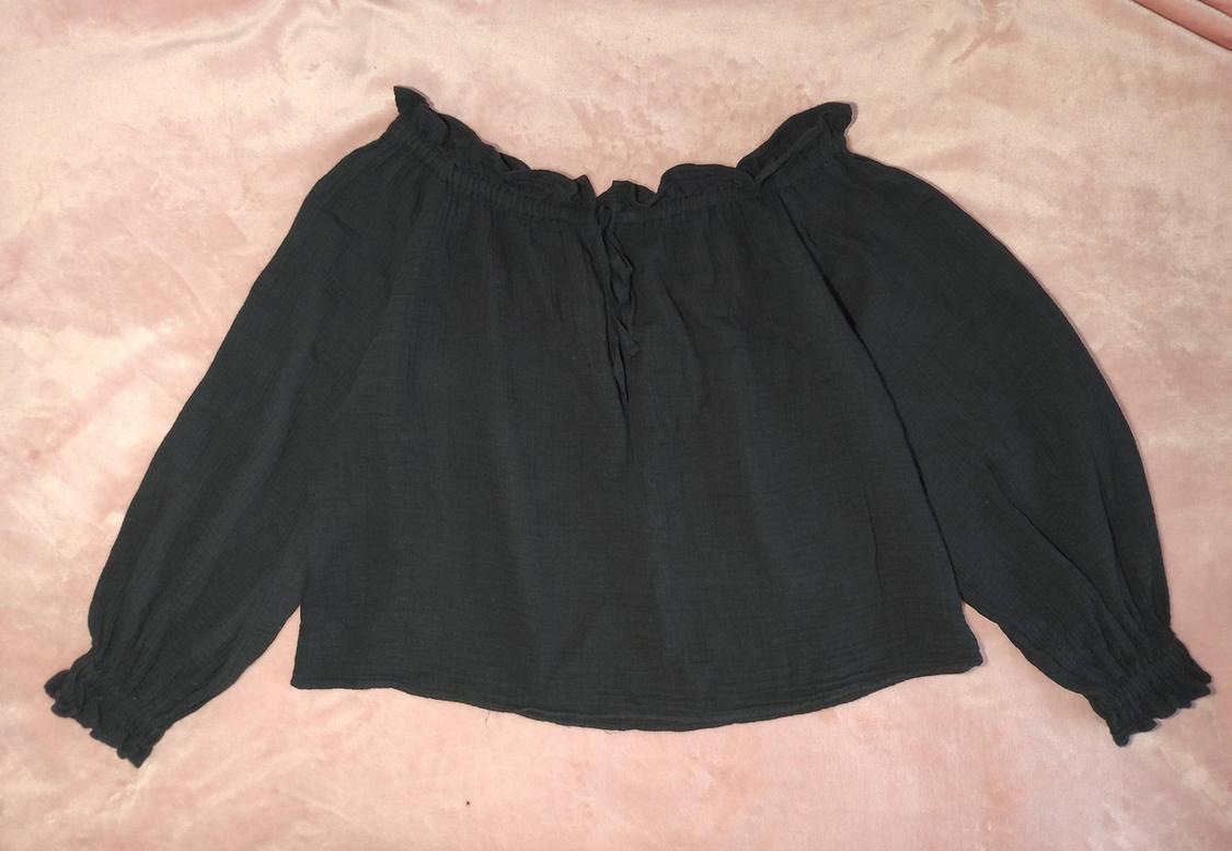 Black long-sleeved blouse with elasticated neckline and ruched details, on a light pink background.