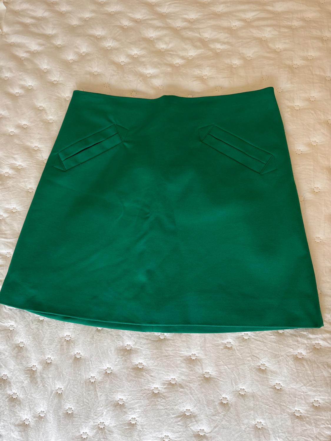 Green skirt on a white bedspread with a floral design. The skirt has two decorative pockets on the front.