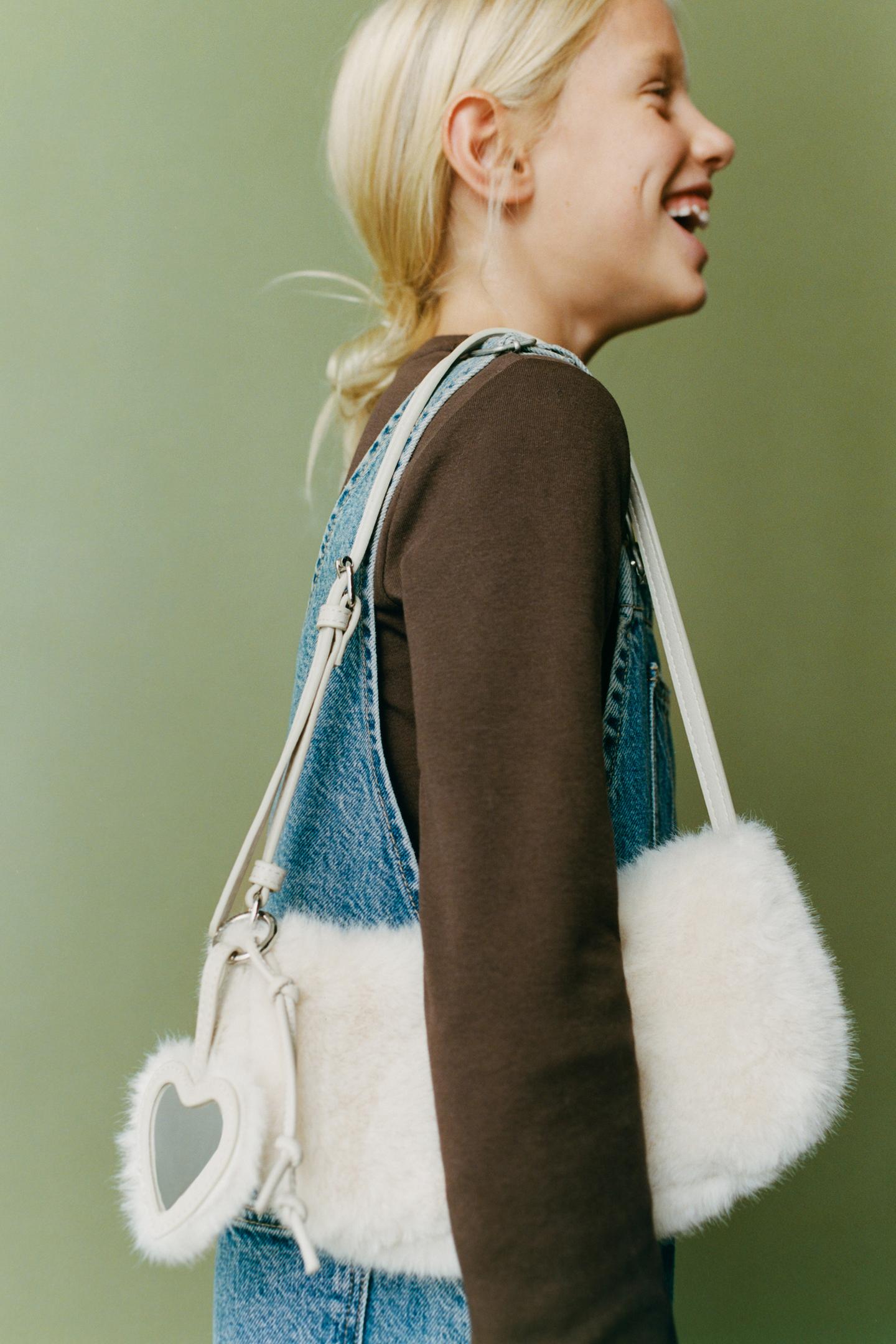 Medium shot of an handbag with a heart-shaped charm and an adjustable shoulder strap.