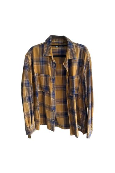 Brown and blue checked shirt with buttons and front pockets, hanging against a white background. Label visible on the collar.