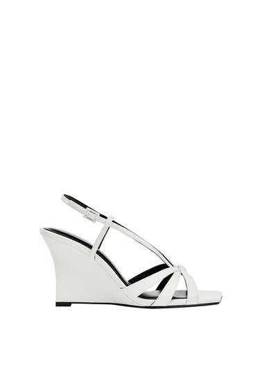 White wedge sandal with thin straps, square toe, black insole, and buckle closure on a white background.