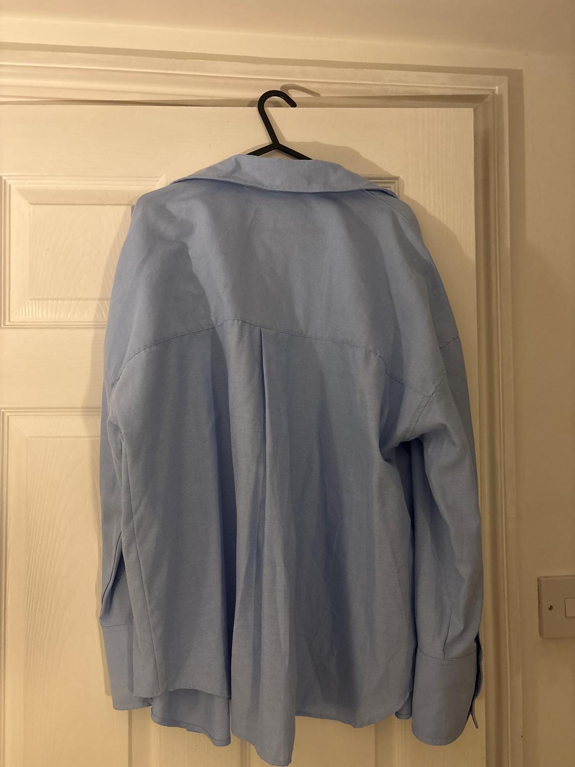 Light blue shirt hanging on a black hanger over a white door. The shirt is viewed from the back.