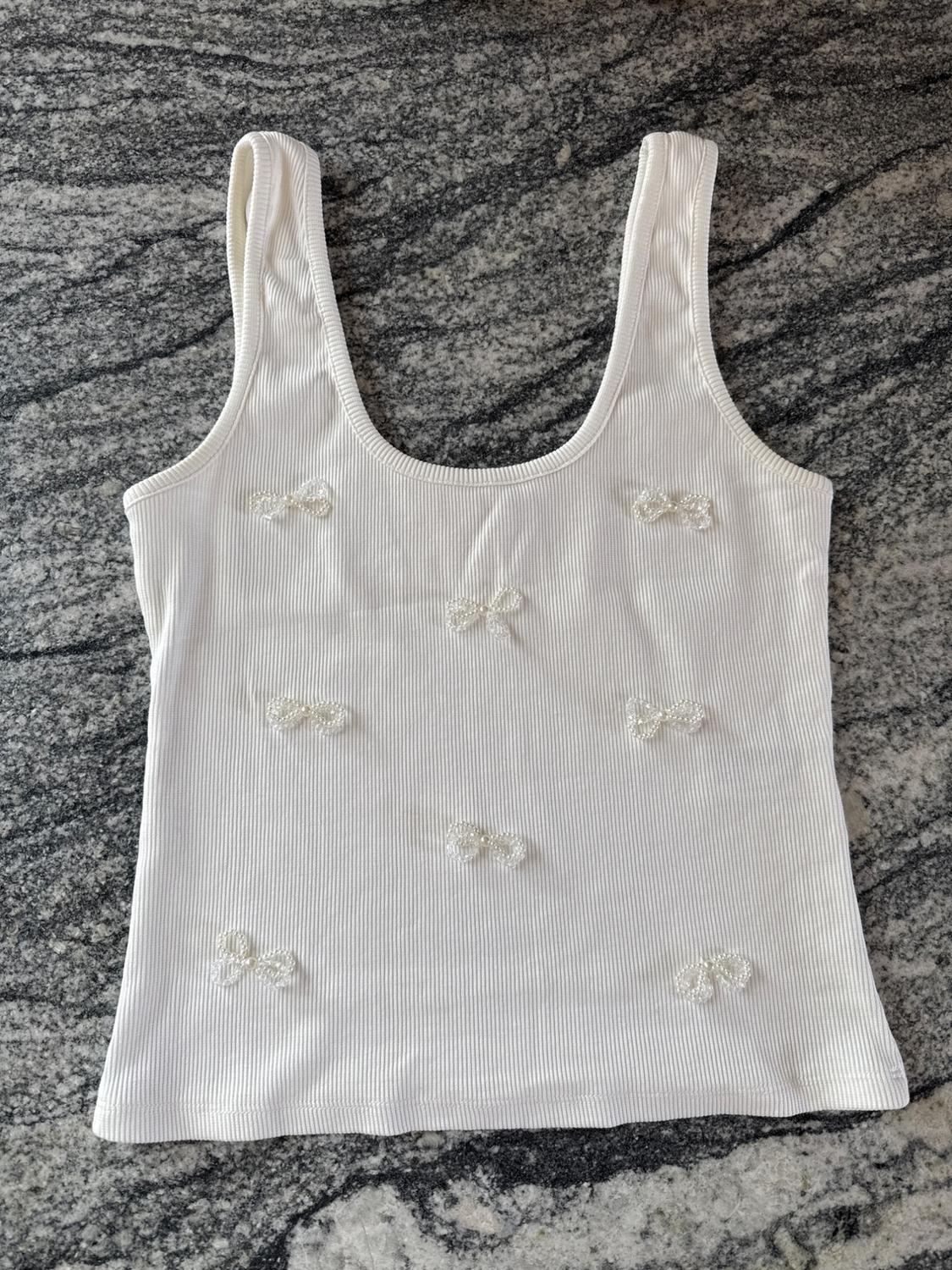 White vest top with pearl-tie detailing, on a grey marble background with dark veining.
