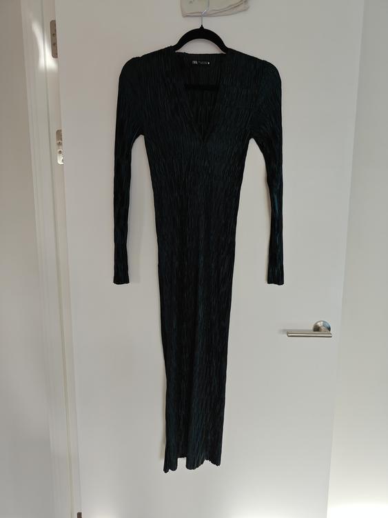 Long black long-sleeved dress hanging on a black hanger over a white door.
