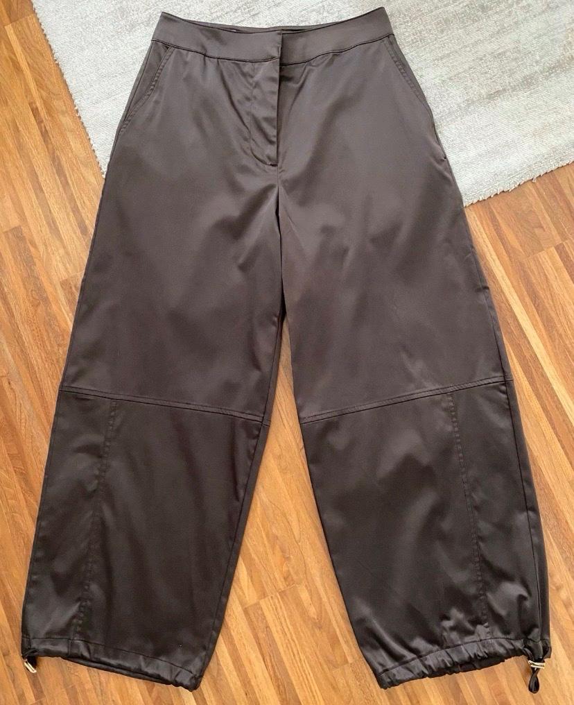 Dark brown wide-leg trousers with stitching and adjustable hems, photographed on a wooden floor and a light-coloured rug.