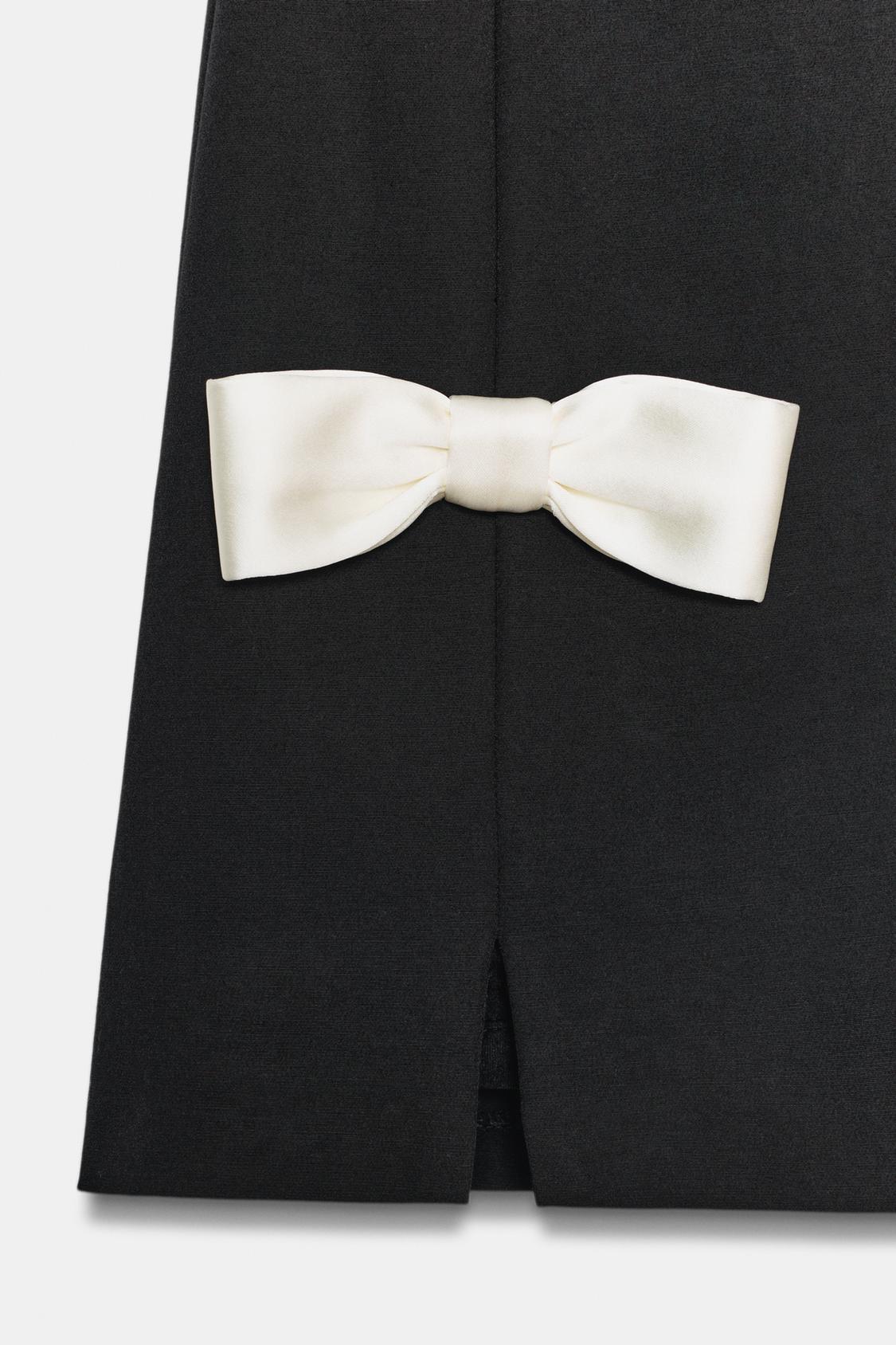 Podrobnost bele mašne na črni obleki s sprednjo odprtino.