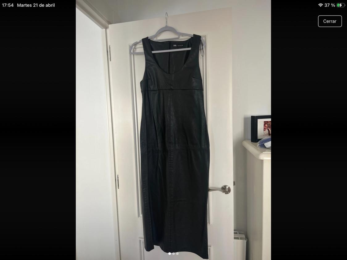 Sleeveless black dress hanging on a white door. Background with a shelf and a photo frame. Text: "Tuesday 21 April".