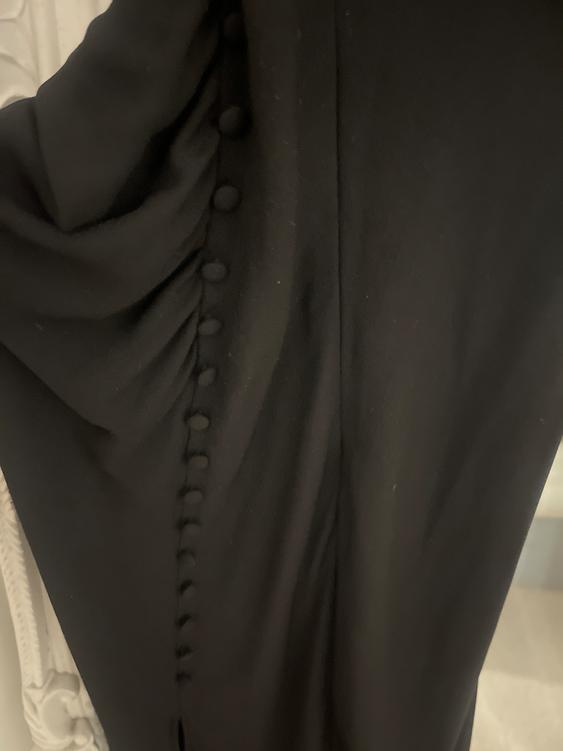Black fabric with covered buttons in a vertical row. The texture is soft and the background is light with decorative details.