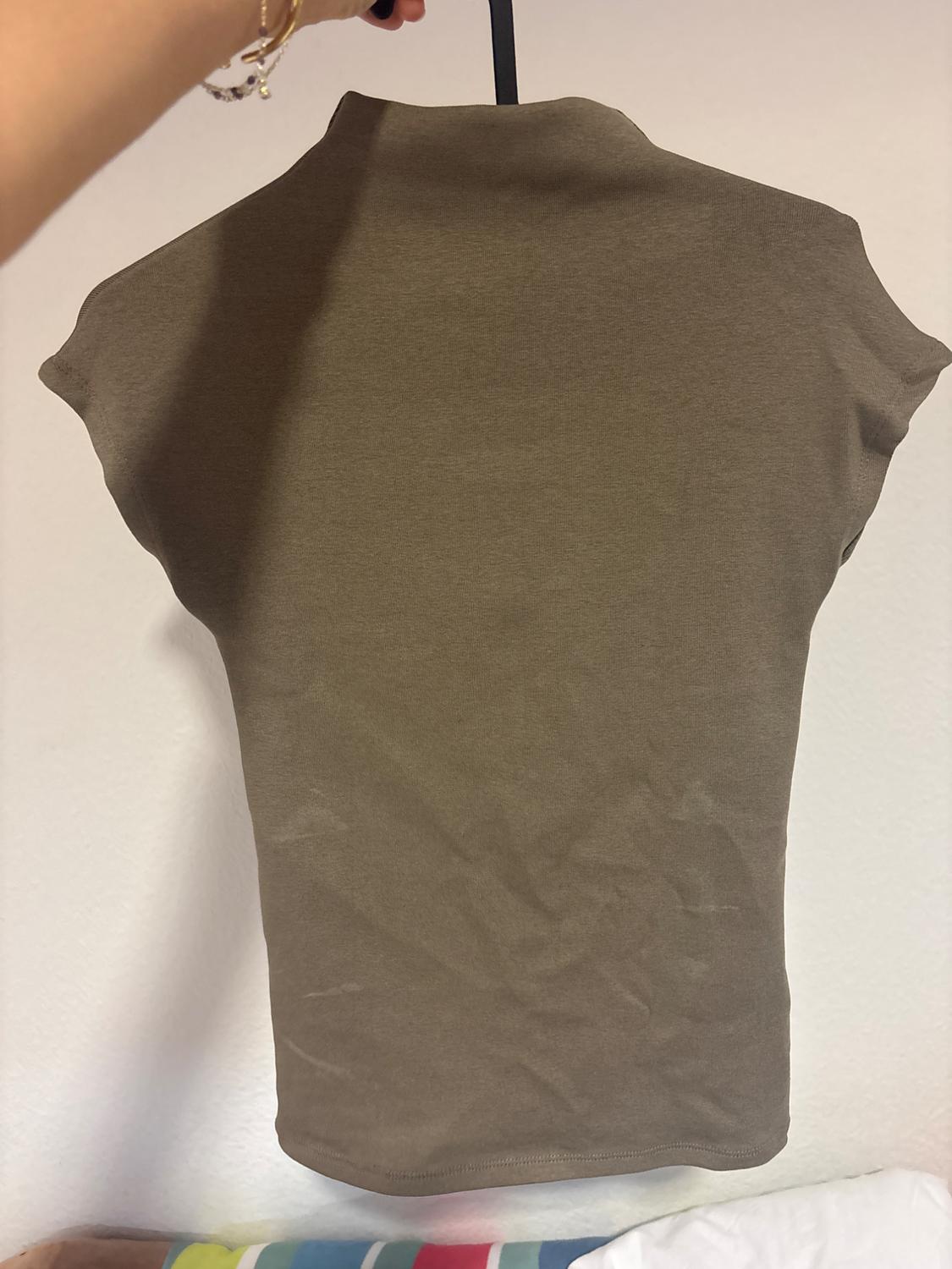 Brown short-sleeved t-shirt hanging on a hanger, viewed from behind. White background and hand holding the hanger.
