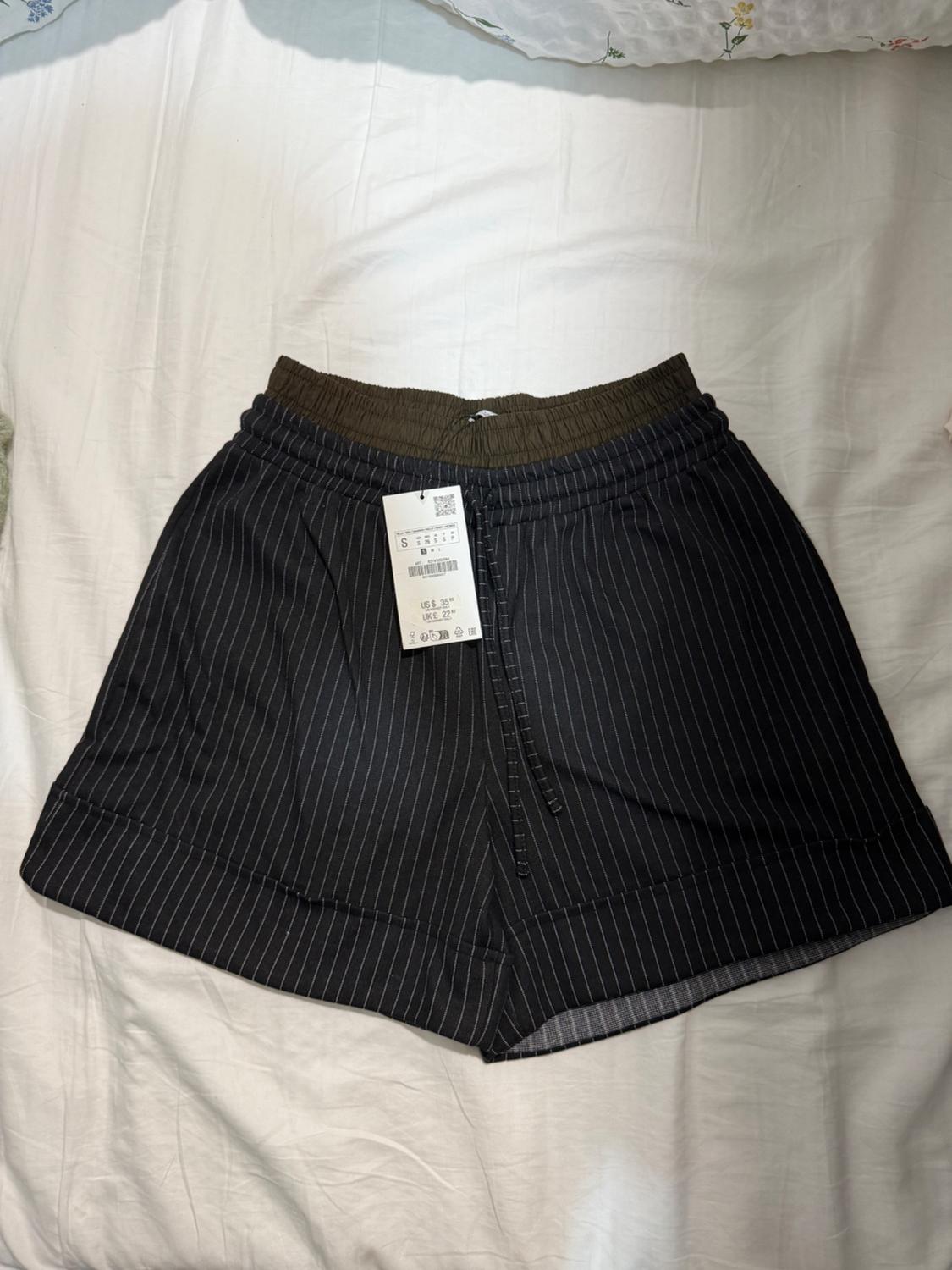 Black striped shorts with a brown elasticated waistband and a dollar price tag on a white bed.
