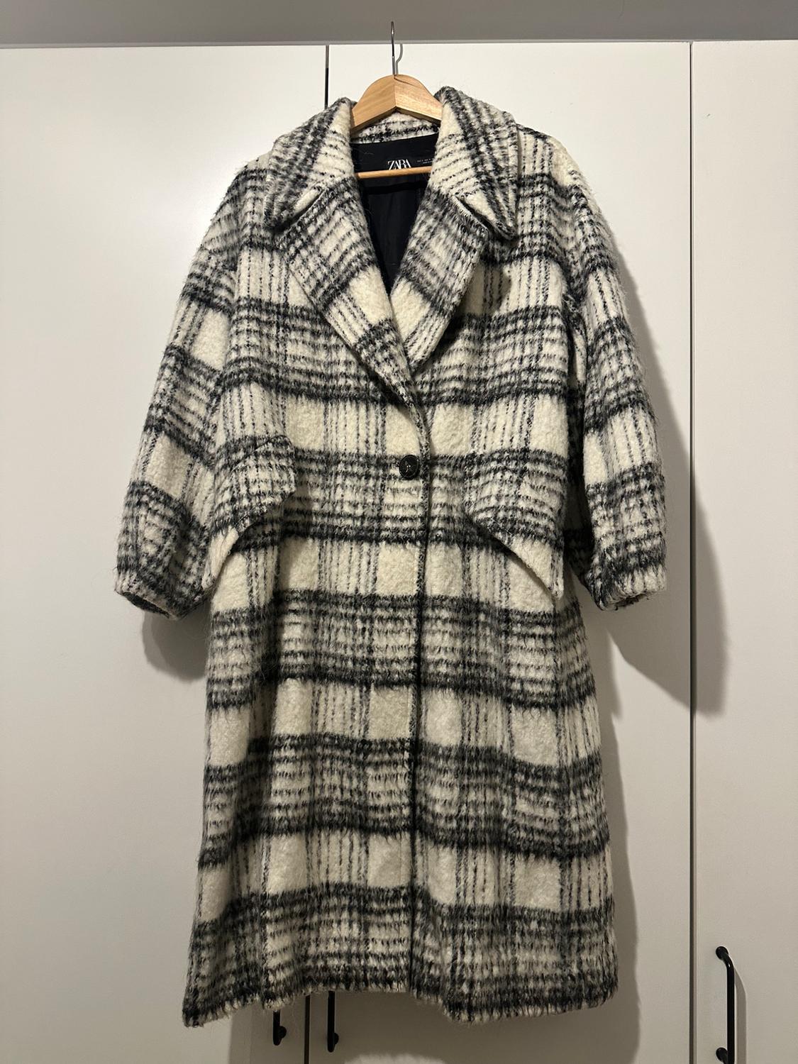 Black and white checked coat hanging on a wooden hanger, against a white wardrobe background.
