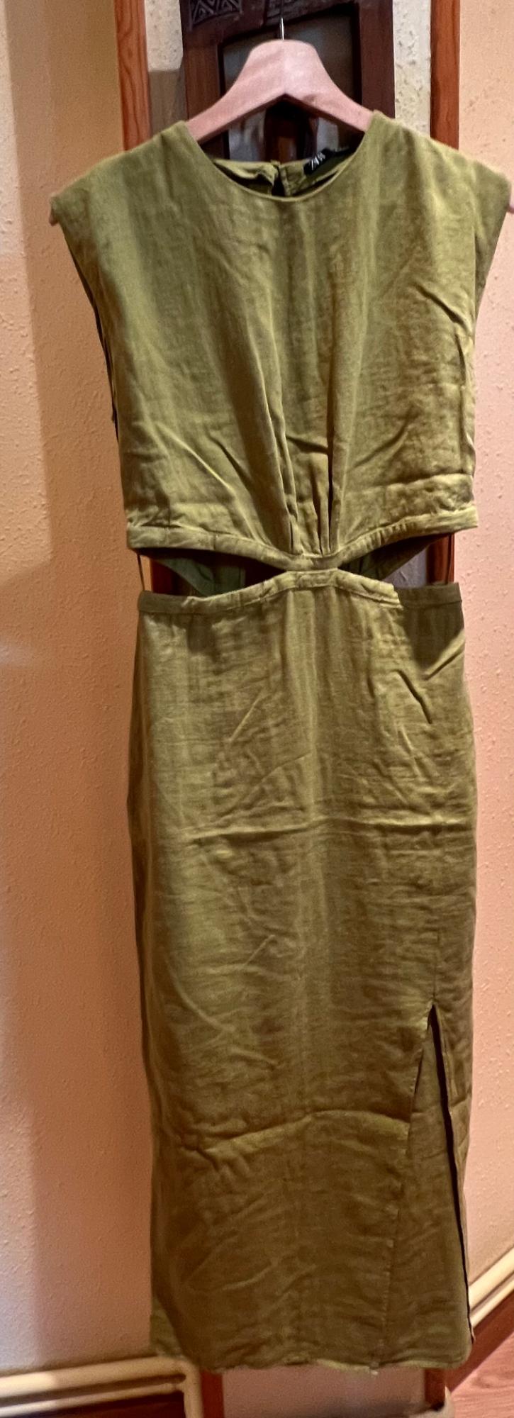 Olive green, sleeveless dress with a side split, hanging on a wooden hanger against a beige background.