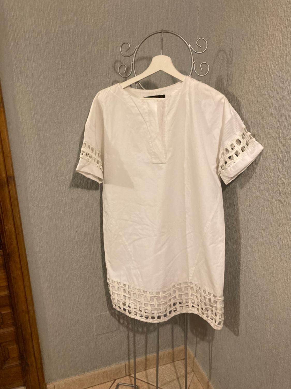 Front view of a white dress with short sleeves and cut-out details on the sleeves and hem.