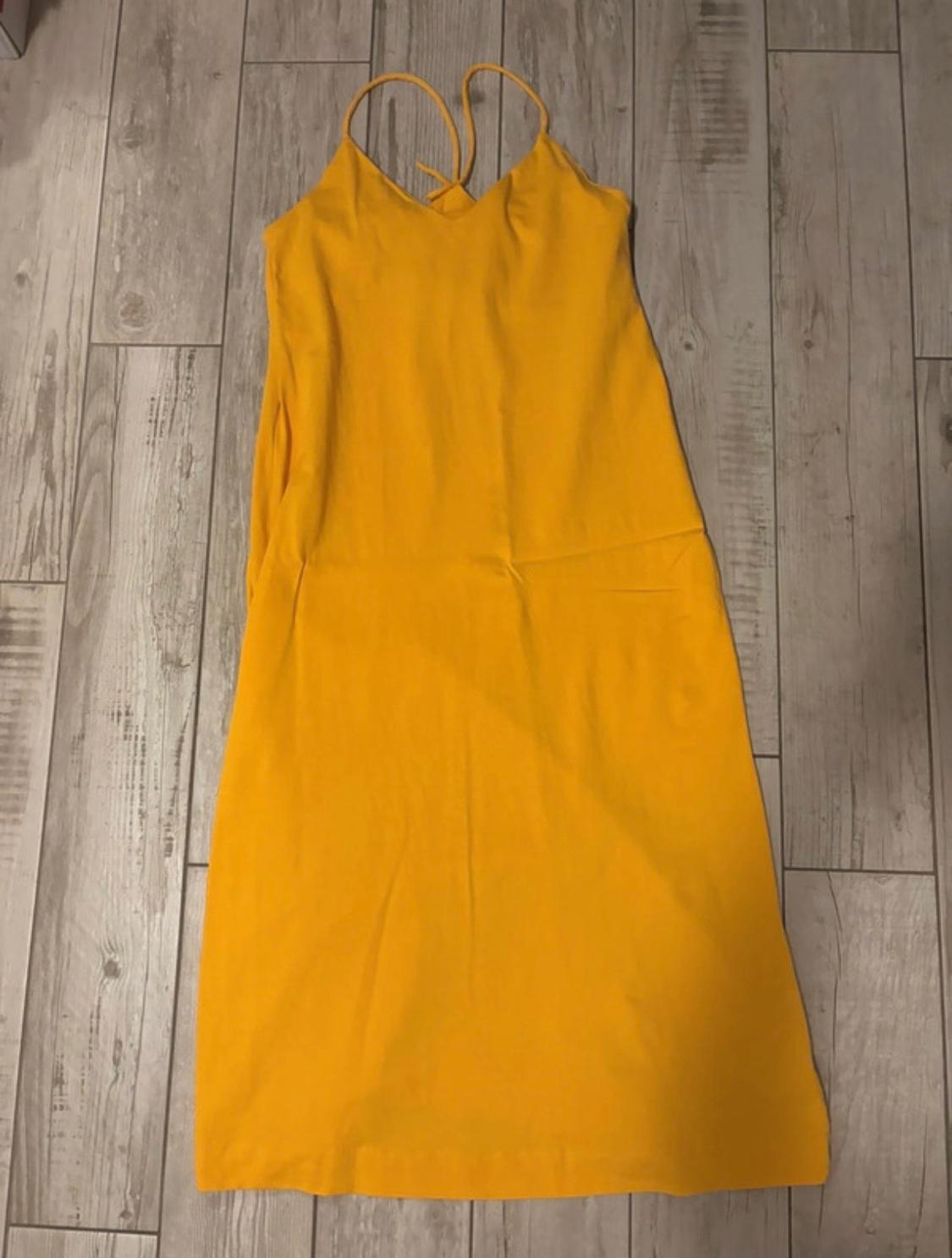 Long yellow dress with thin straps and a V-neckline, laid out on a light wooden floor.