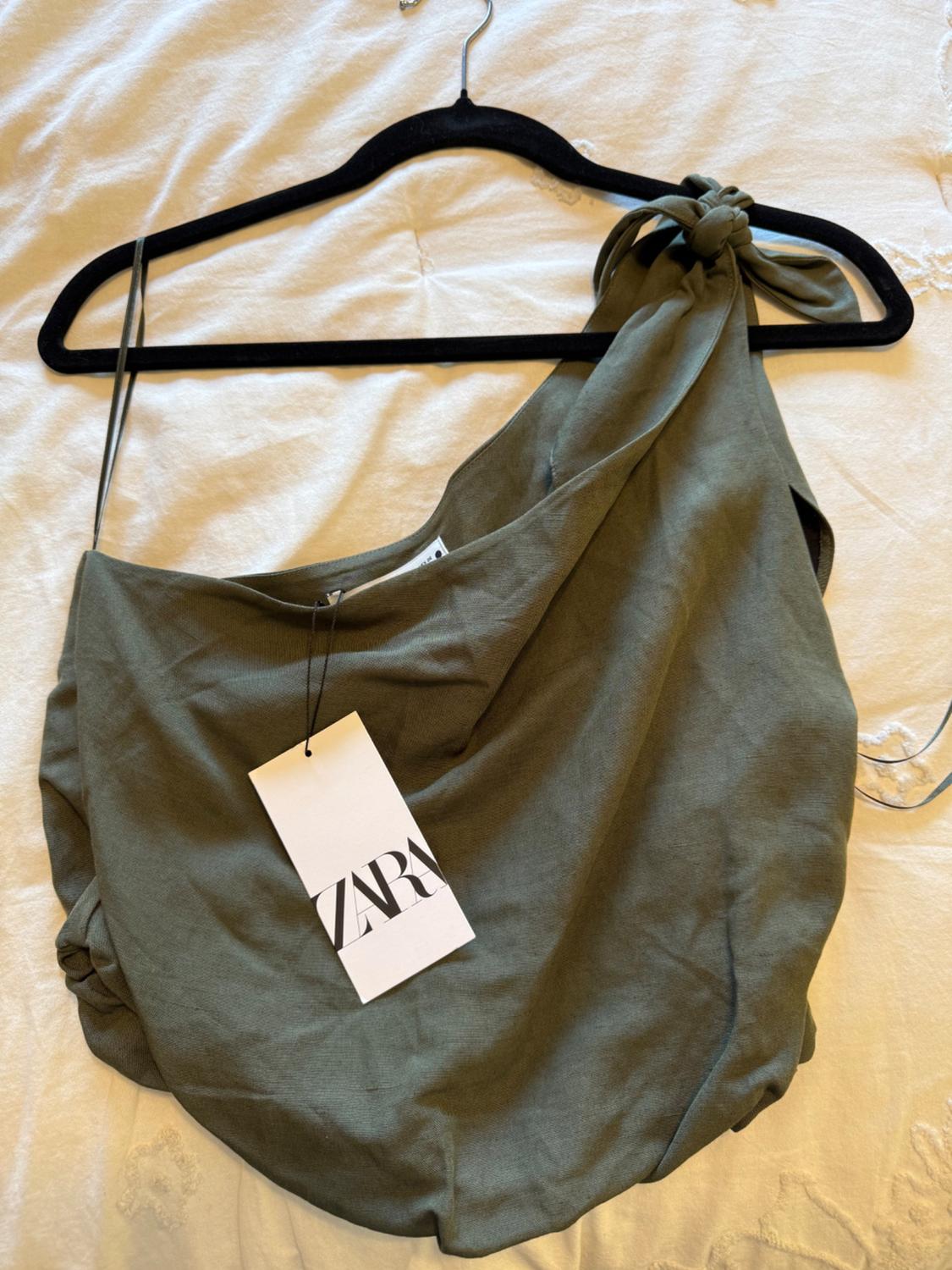 Olive green one-shoulder top with a knot on the strap, hanging on a black hanger. White label with "ZARA" text.