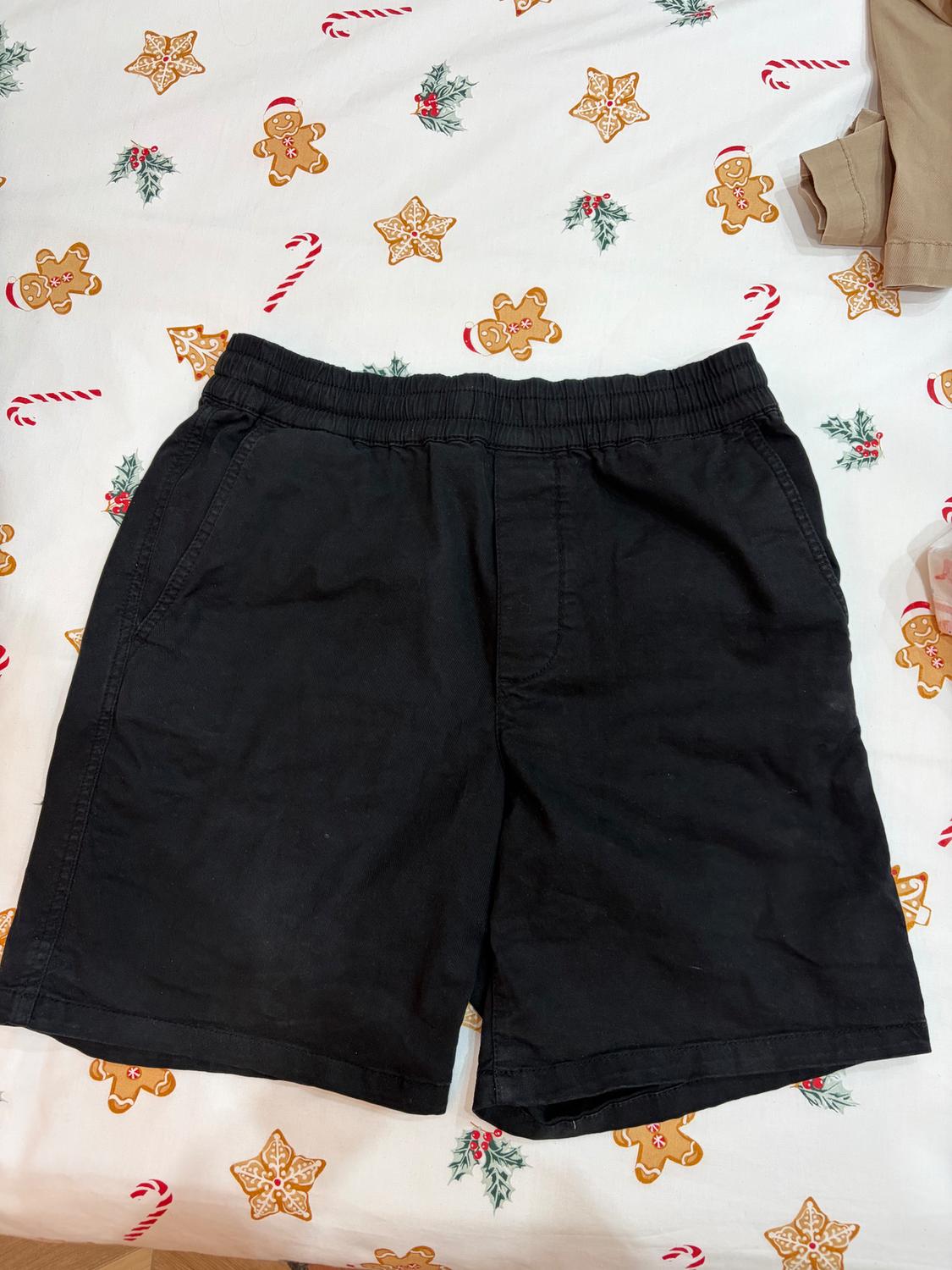 Black shorts on a Christmas-themed sheet with a print of gingerbread men, candy canes, and holly leaves.