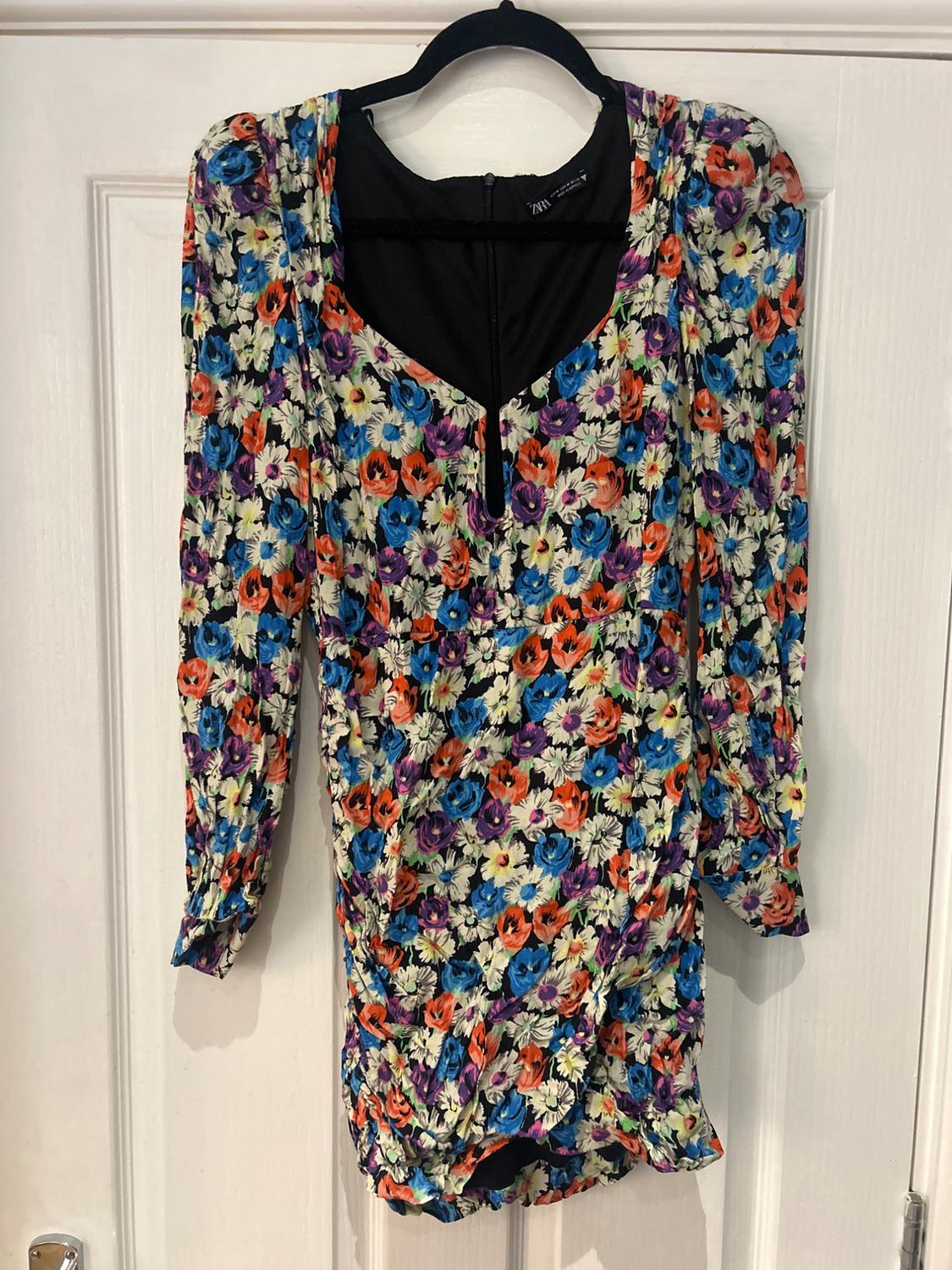 Multicoloured floral dress with long sleeves and V-neck, hanging on a black hanger over a white door.