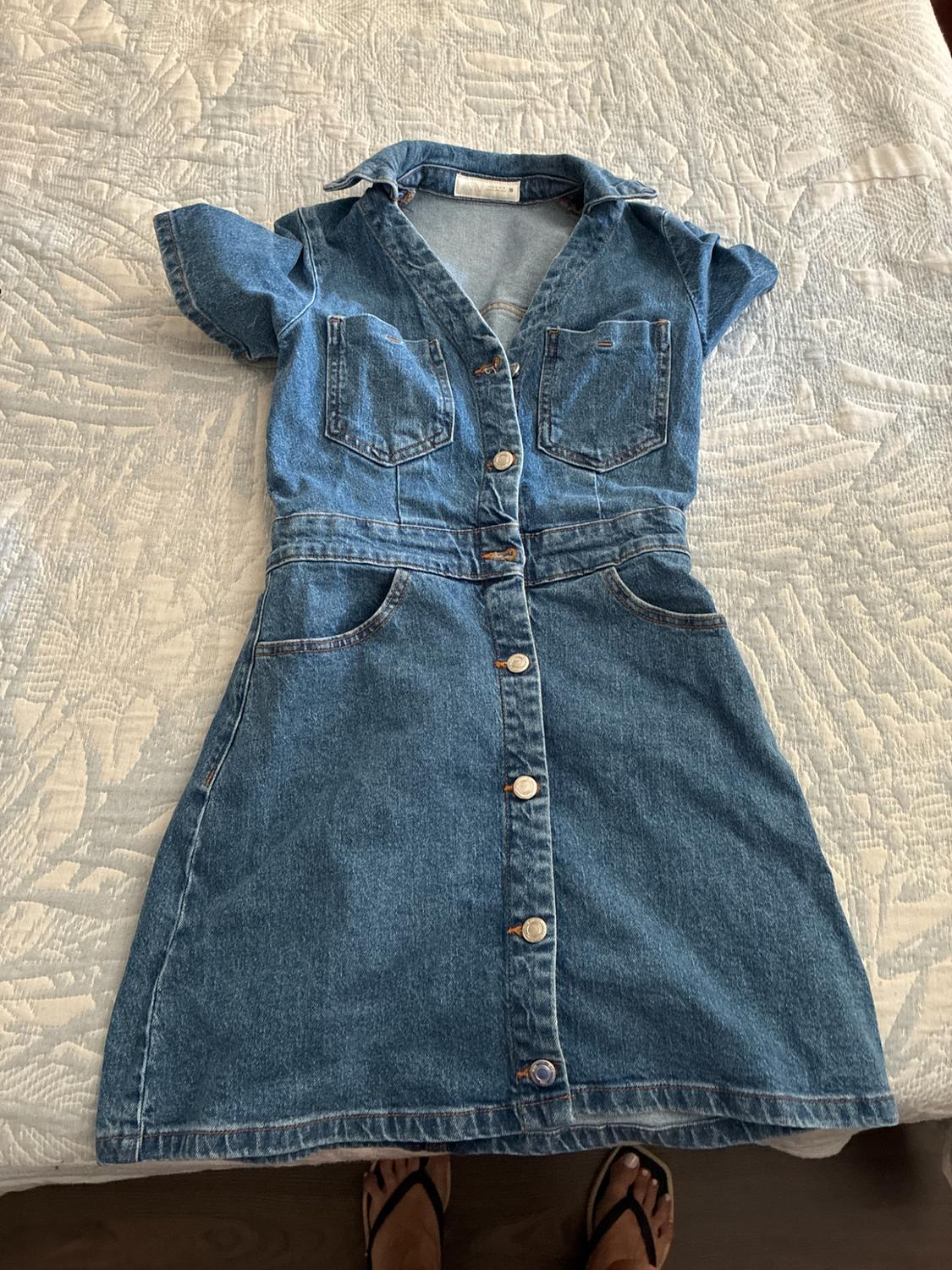 Short-sleeved denim dress with front buttons and pockets, on a light patterned bedspread.
