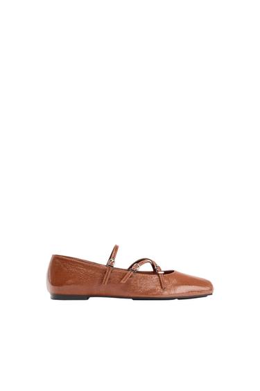 Brown flat shoe with a glossy finish and thin straps, on a white background.