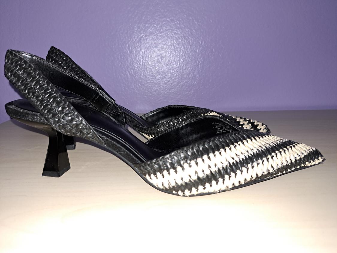 Black and white low-heeled shoes with a braided design, on a light surface and lilac background.