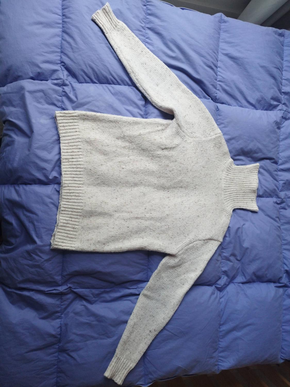 Light grey knitted roll-neck jumper, laid out on a quilted blue duvet.