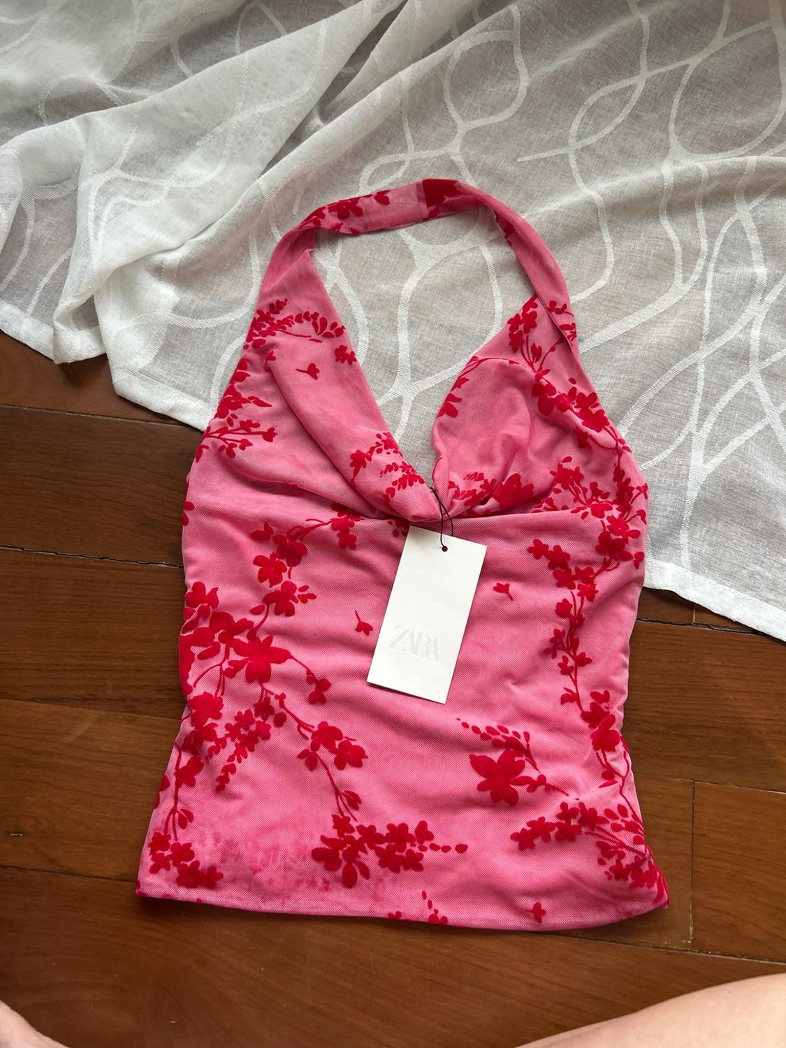 Pink halterneck top with a red floral print and ZARA label, on a wooden floor and white fabric.