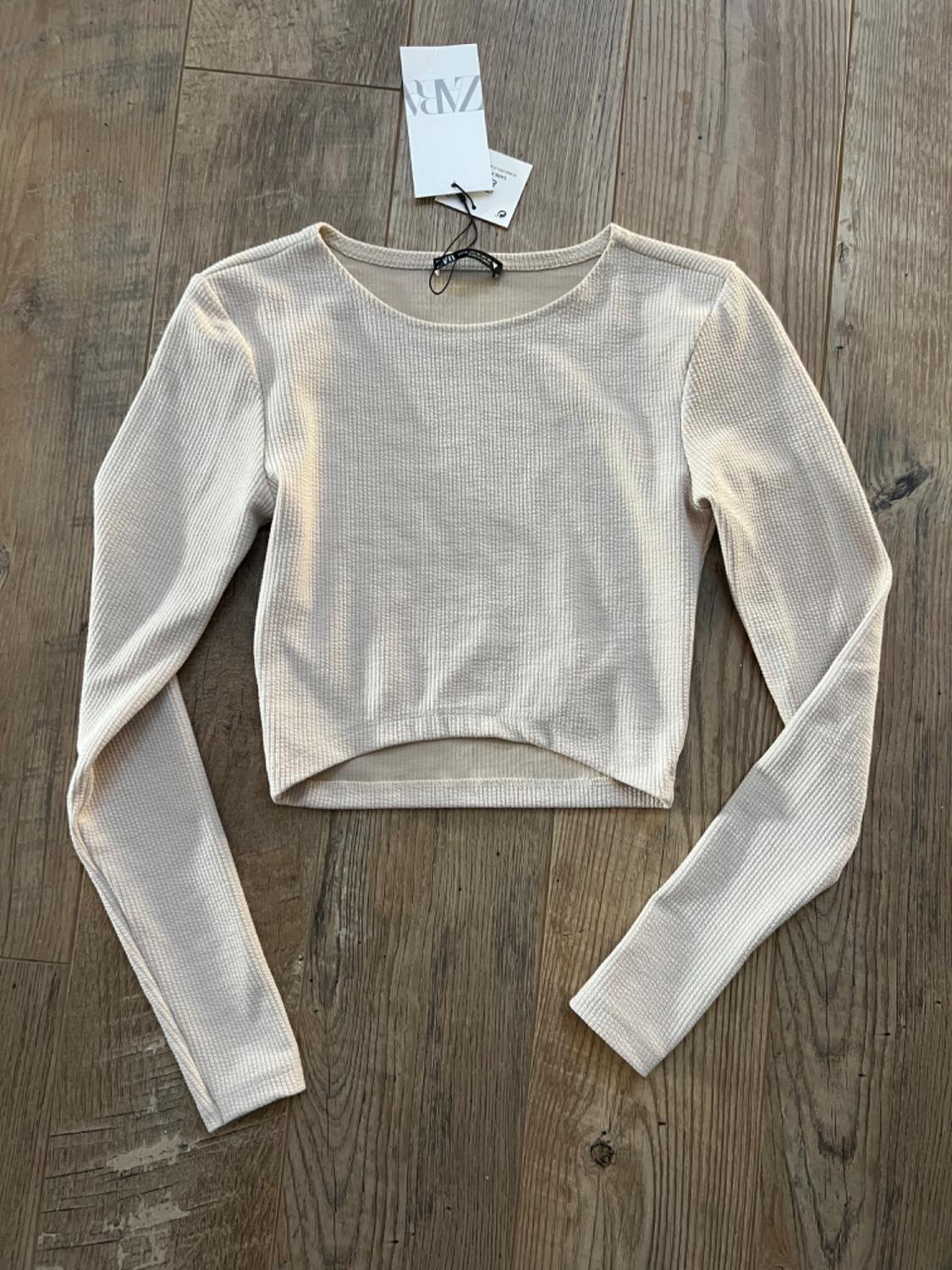 Front view of a beige long-sleeved, crew-neck top with a ribbed texture and cropped cut.