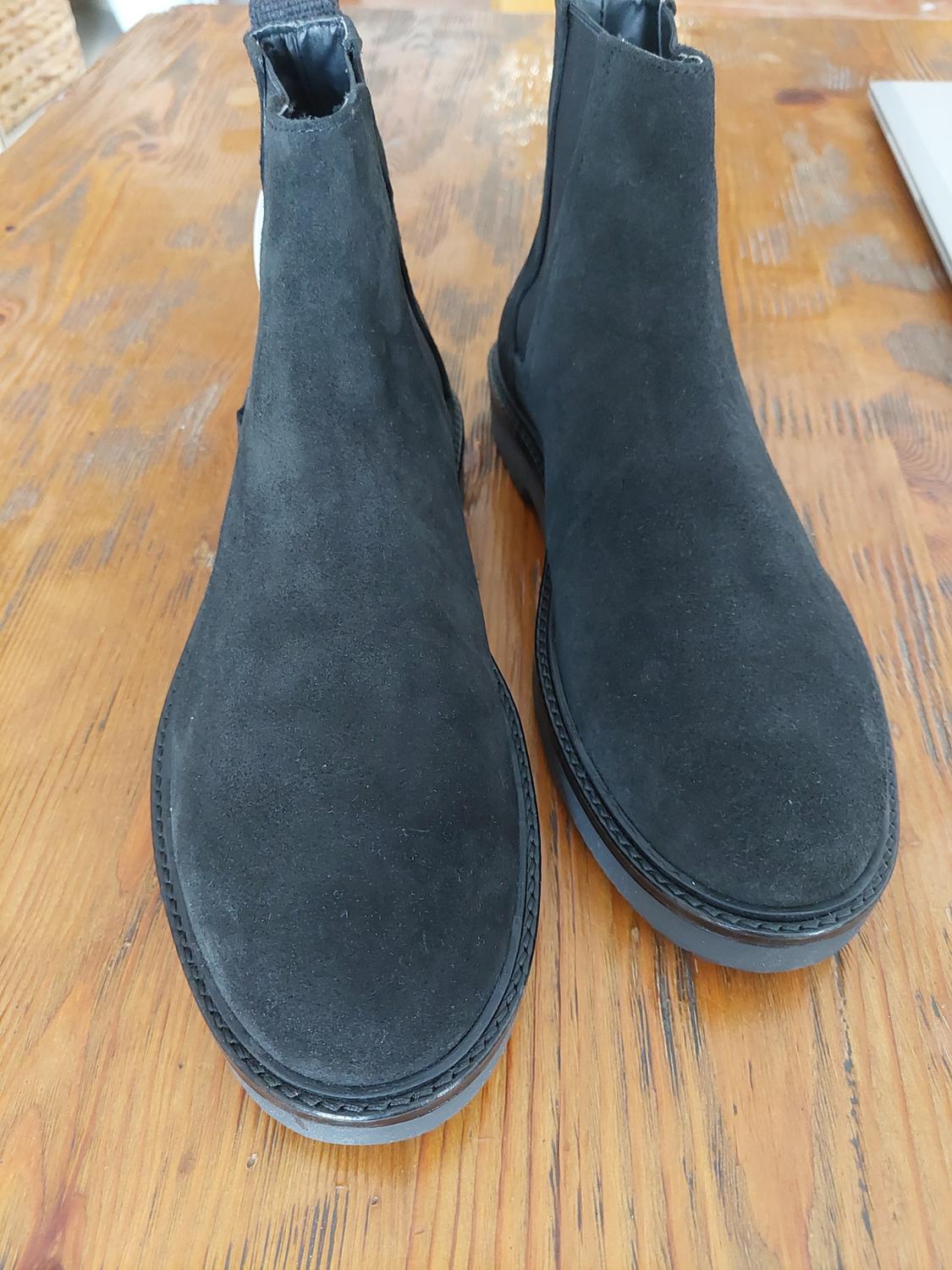 Black suede boots on a light wooden table. The image shows a pair of boots from the front.