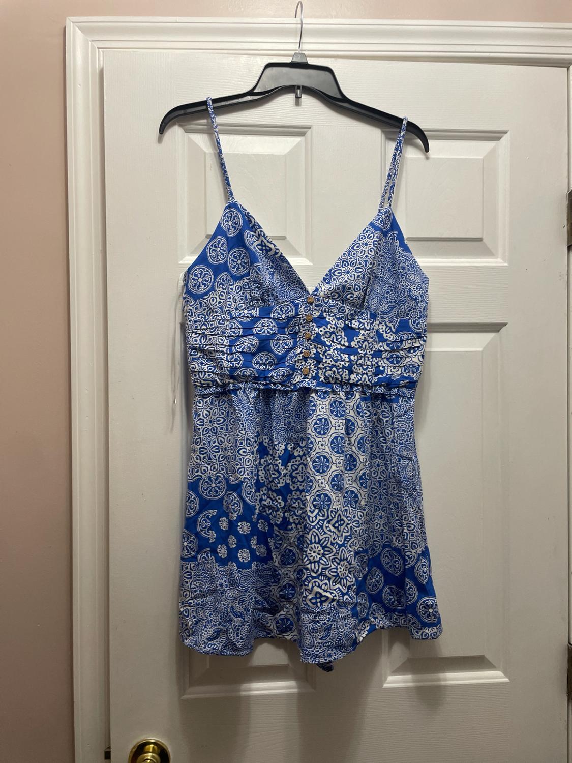 Short blue and white print spaghetti strap dress with front buttons, hanging on a hanger over a white door.