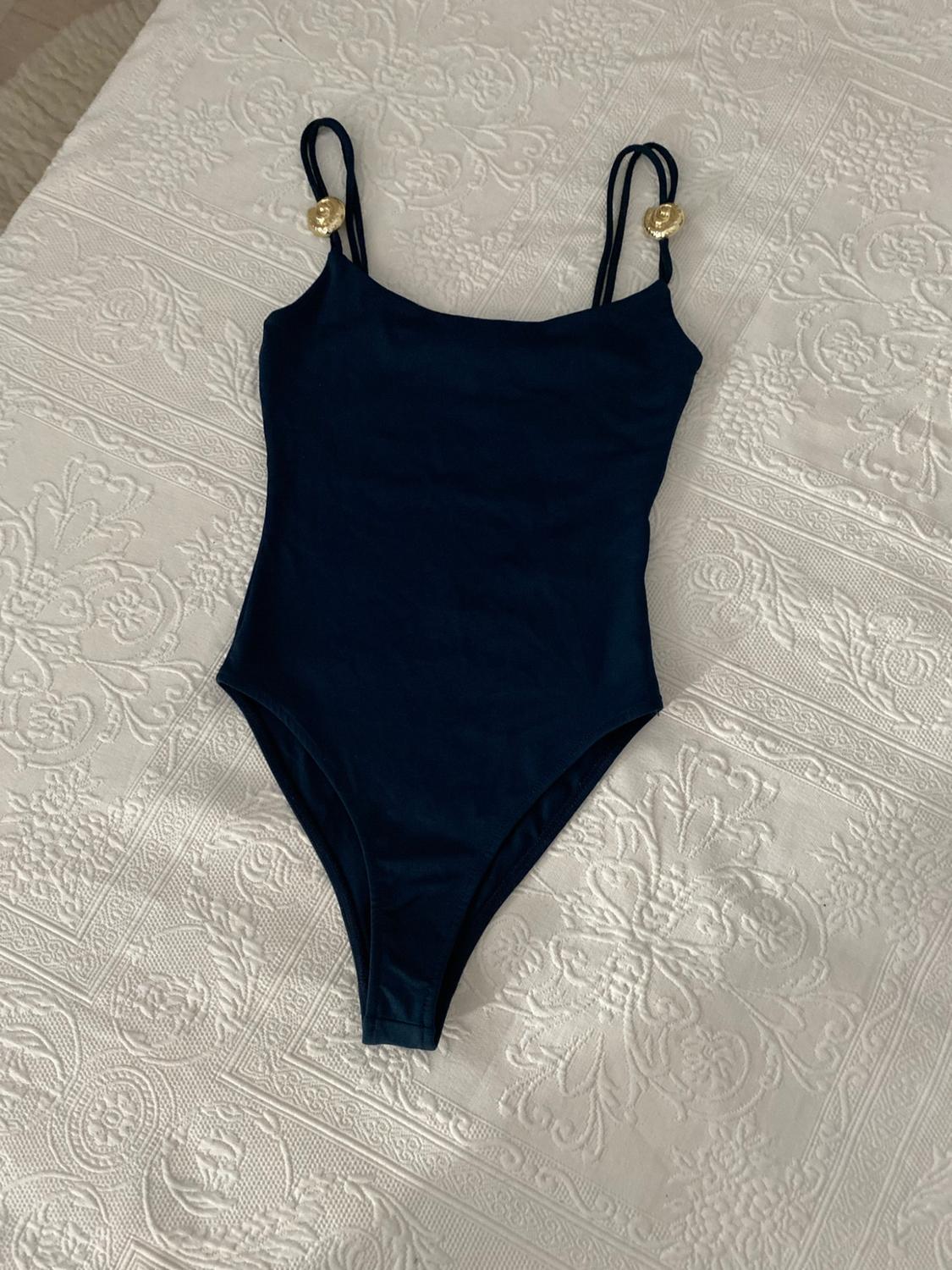Navy blue swimsuit with double straps and gold details, on white fabric with a floral texture.