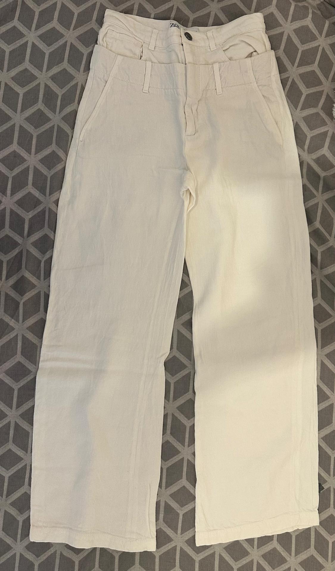Lightweight white trousers with front pockets and belt loops, placed on a grey quilt with a geometric pattern.