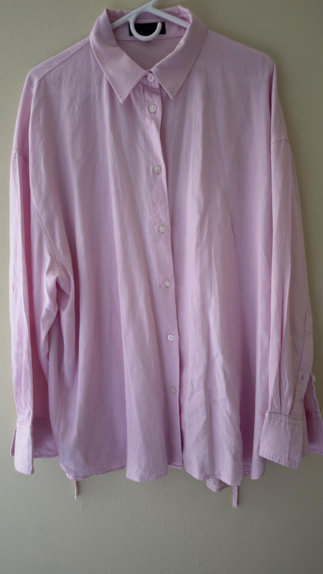 Loose-fitting light pink shirt hanging on a white hanger, with front buttons and classic collar.