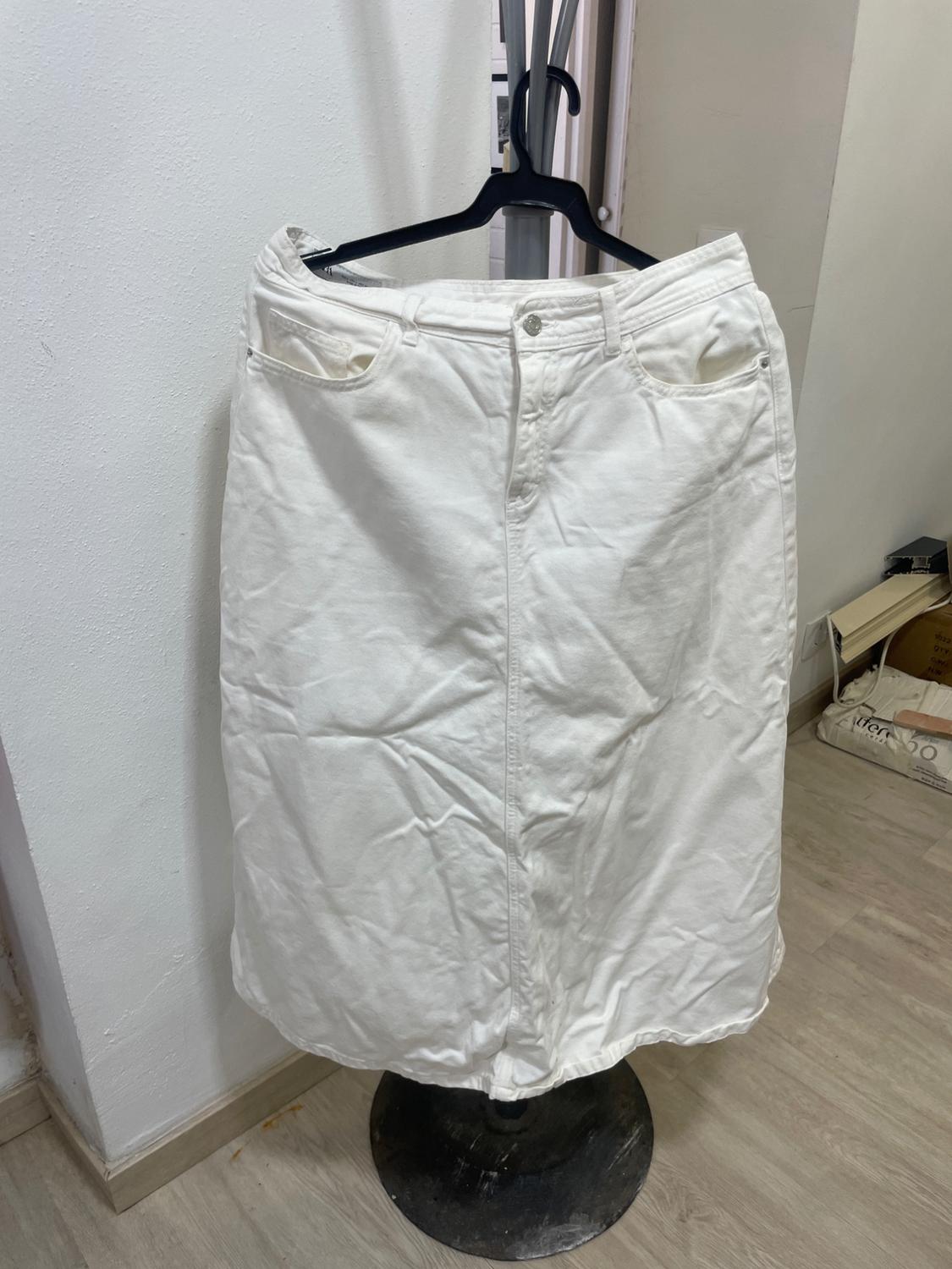 White denim skirt hanging on a black hanger, against a backdrop of a white wall and light wood floor.