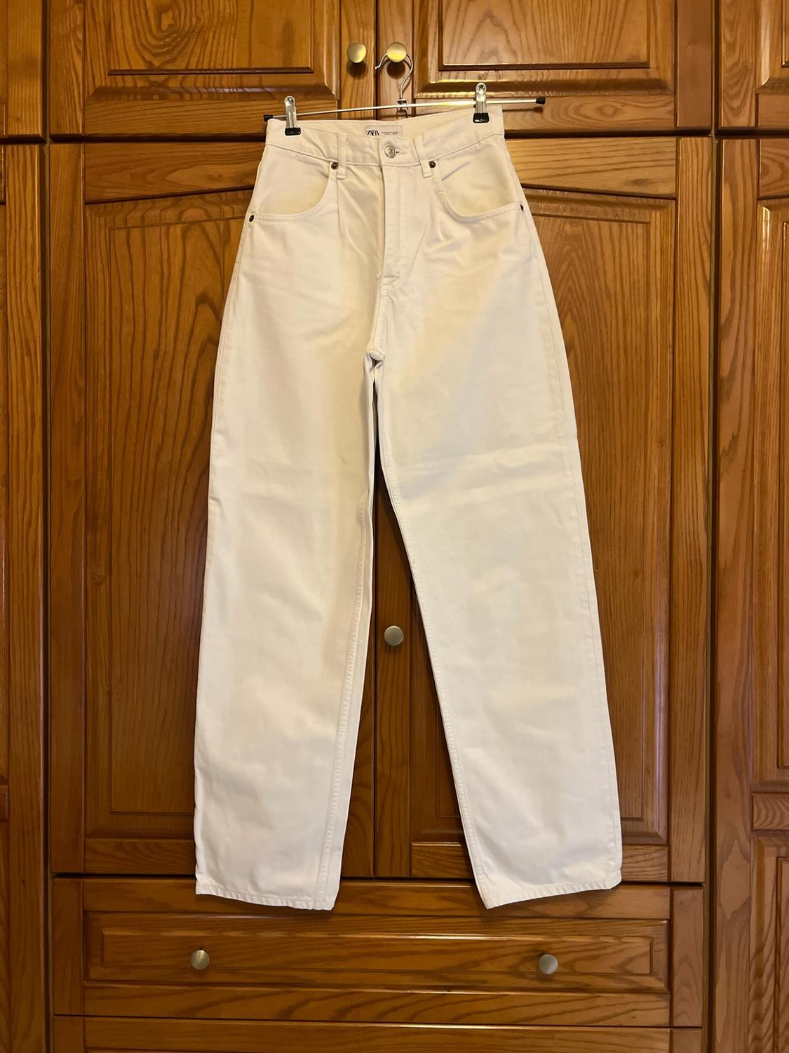 White jeans with a Zara label hanging on a hanger on the doors of a wooden wardrobe. Homely and casual atmosphere.