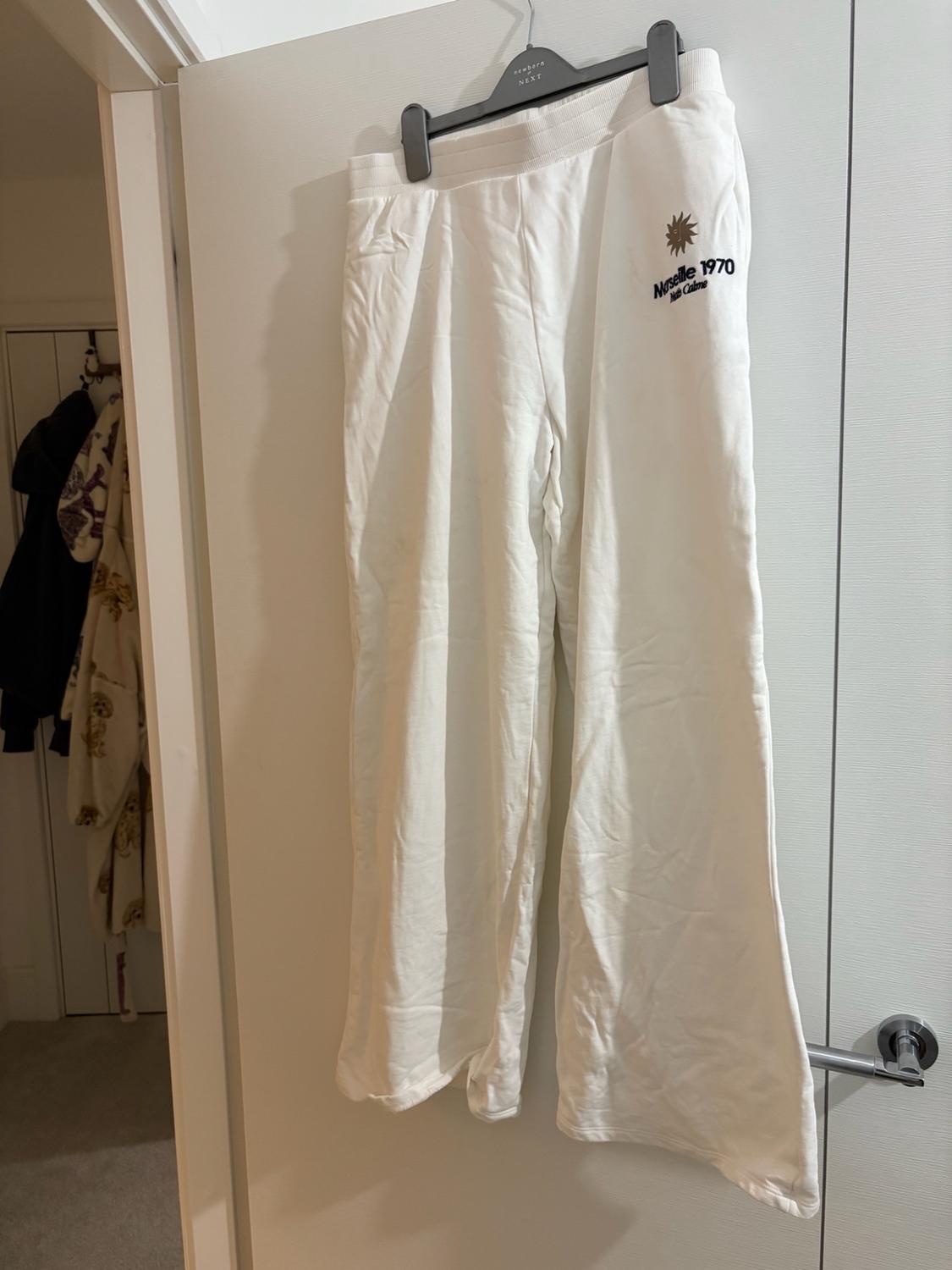 White trousers on a hanger with “newborn NEXT” text hanging on the door. Sun print and “Marseille 1970 Midi Calme” text. Background with clothing.