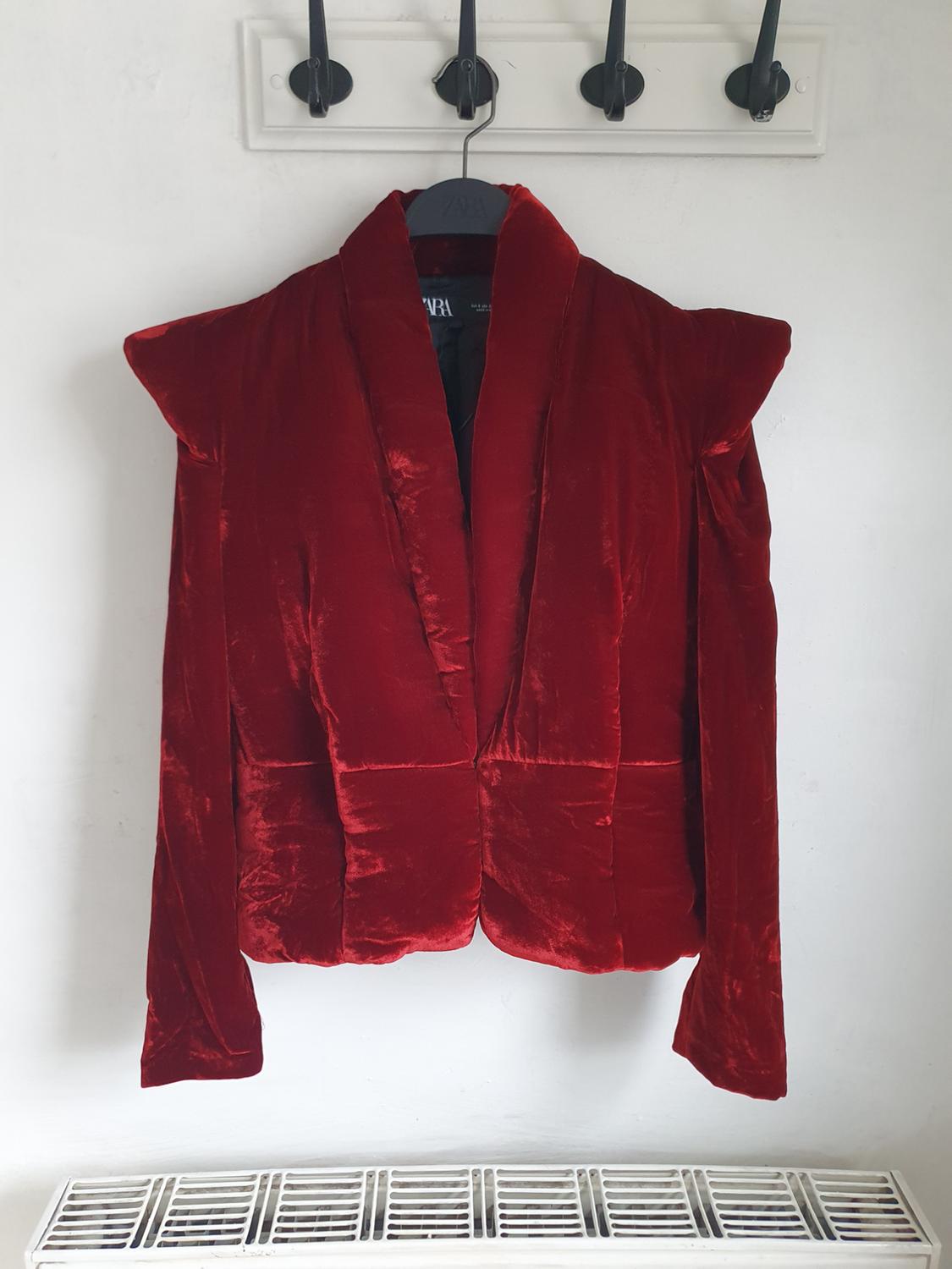 Red velvet jacket with shoulder pads hanging on a black hanger against a white background. Visible label: Zara.