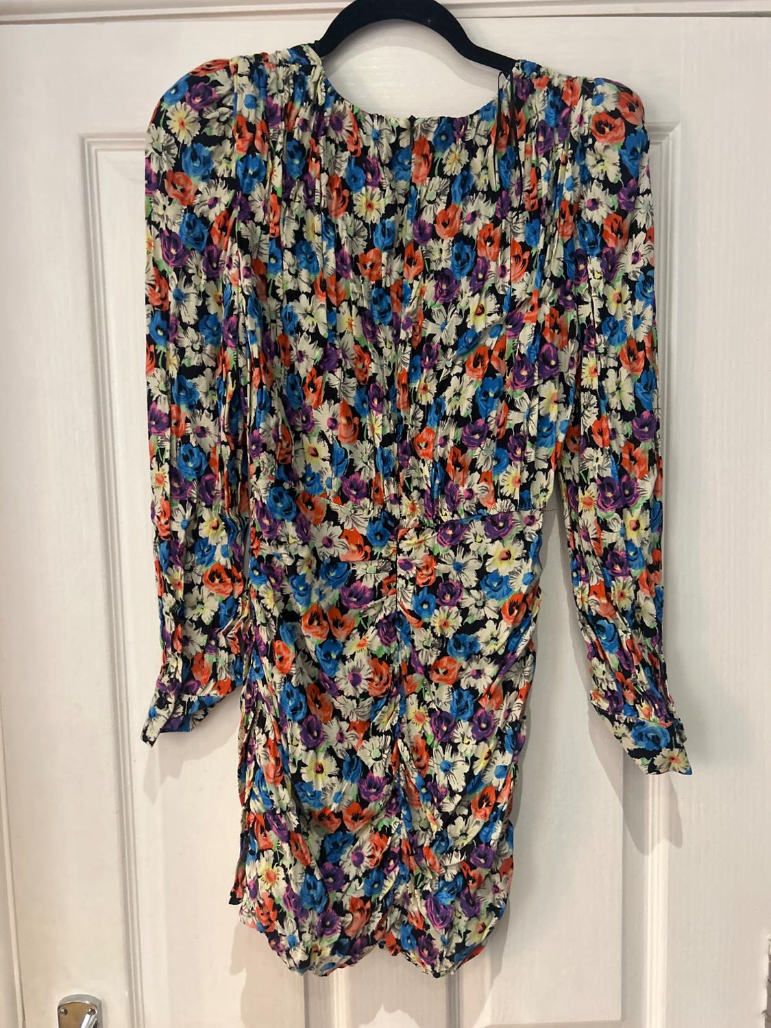 Multicoloured floral print long-sleeved dress, hanging on a black hanger over a white door.