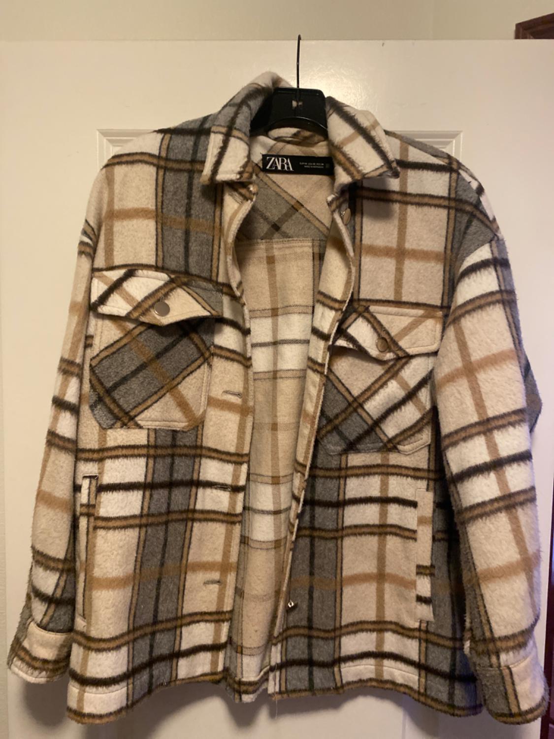 Brown, grey, and white checked jacket hanging on a black hanger. Visible label with the text "ZARA".