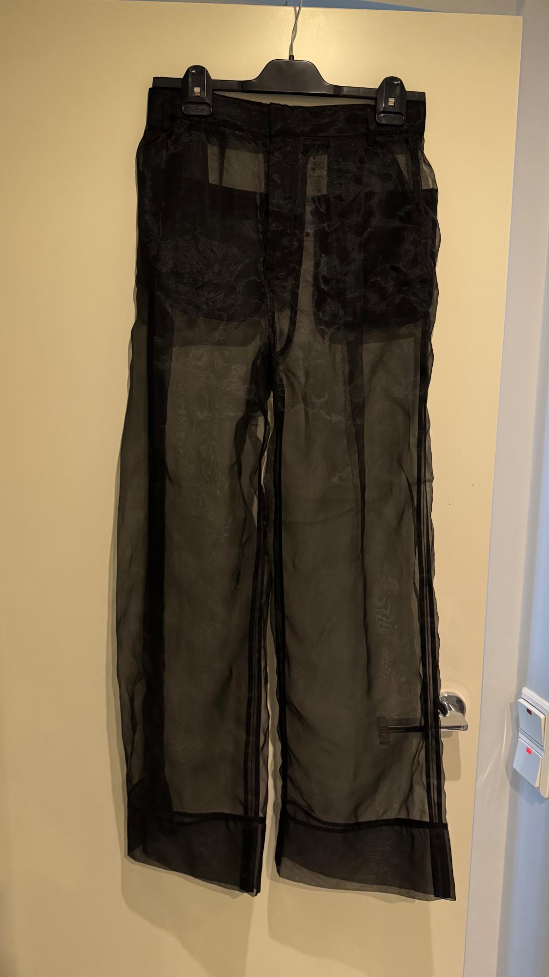 Sheer black trousers hanging on a light-coloured door. The opaque top pockets and dark stripes on the hems stand out.